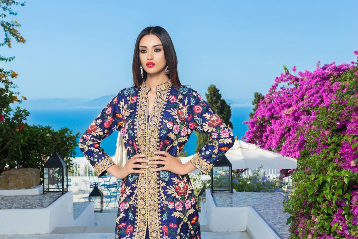 a woman in blue floral long sleeve dress standing near purple flower